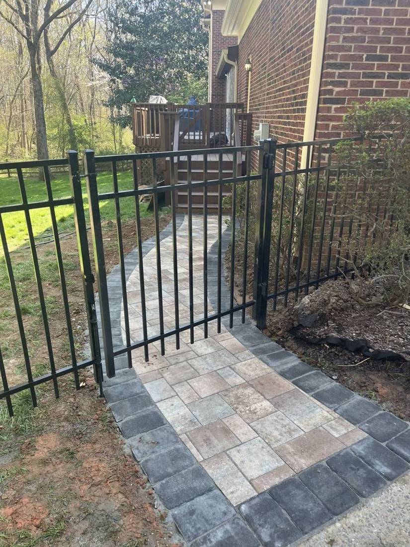 Paver walk with charcoal border through a black metal gate
