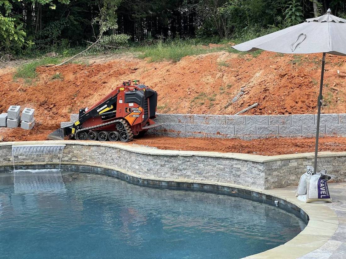 Mini skid steer grading the slope behind a pool as the first wall goes in